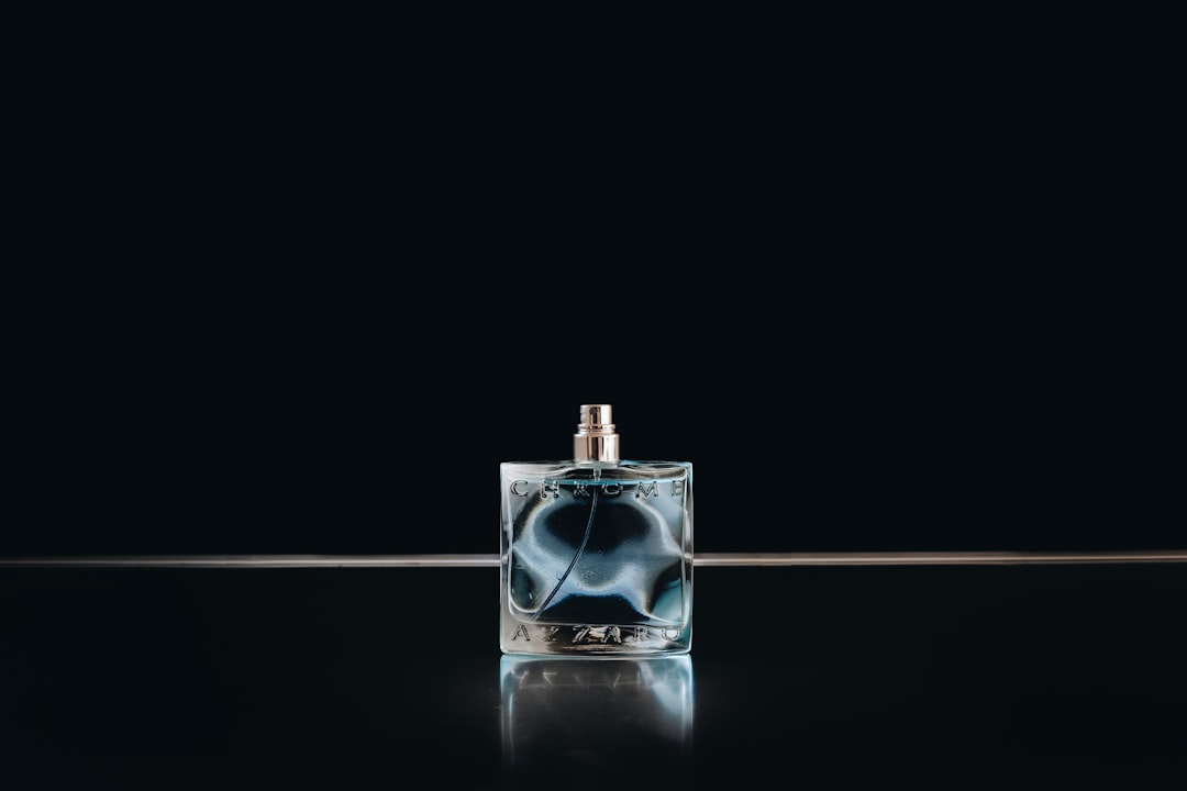 A close-up of a person applying perfume from a stylish bottle, with a soft focus on the background to emphasize the act of fragrance application.