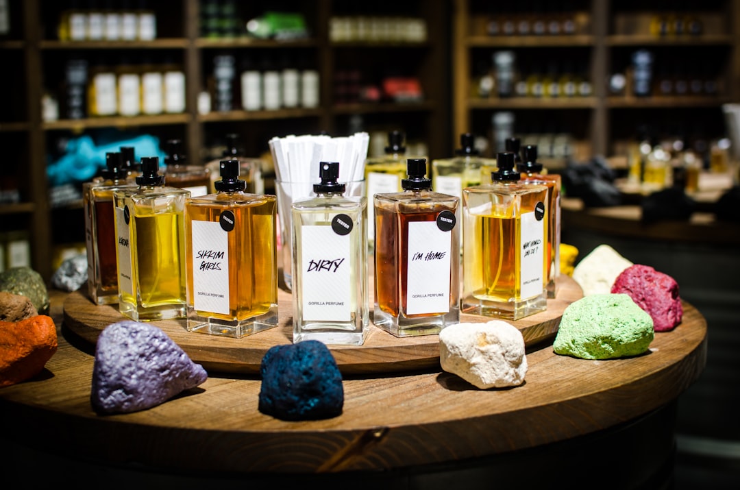 A person holding a perfume bottle with a tester strip, surrounded by various fragrance bottles on a table.